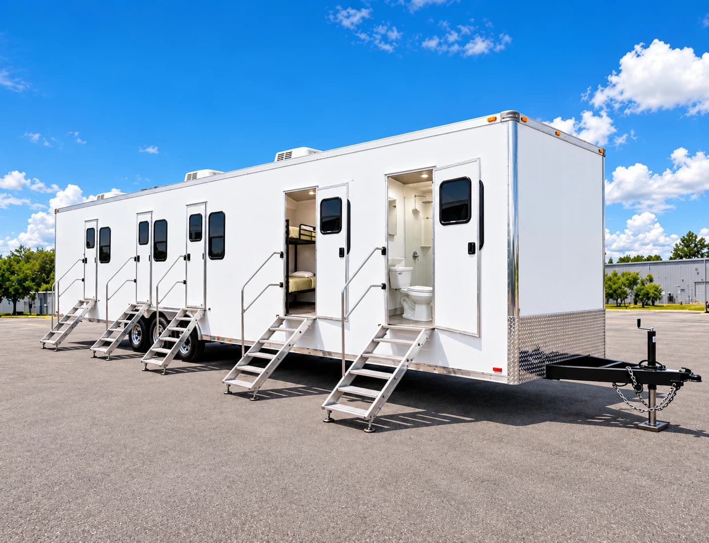 Long white camp trailer with stepped entrances and open doors showing sleeping and hygiene spaces