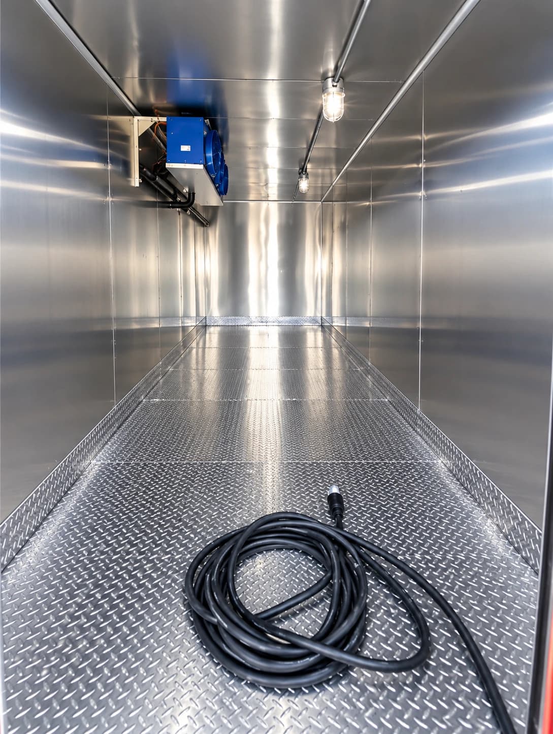 Metal-lined refrigerated trailer interior with a cooling unit above and a coiled cable on the floor