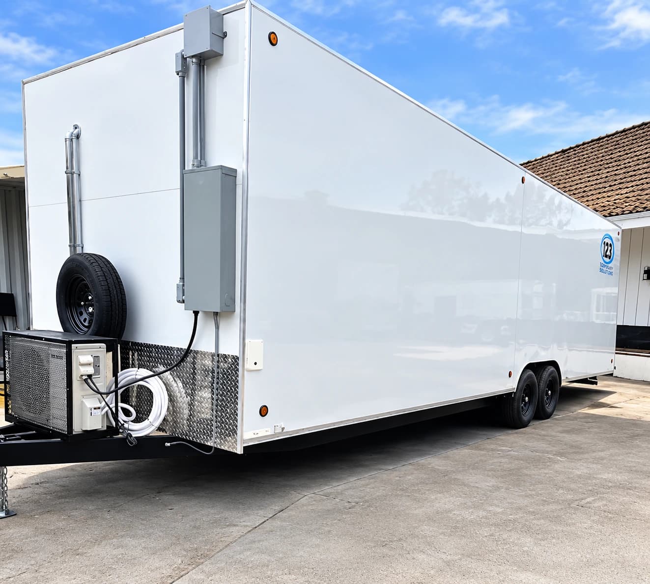 White enclosed tandem-axle trailer with a spare wheel beside the tow hitch