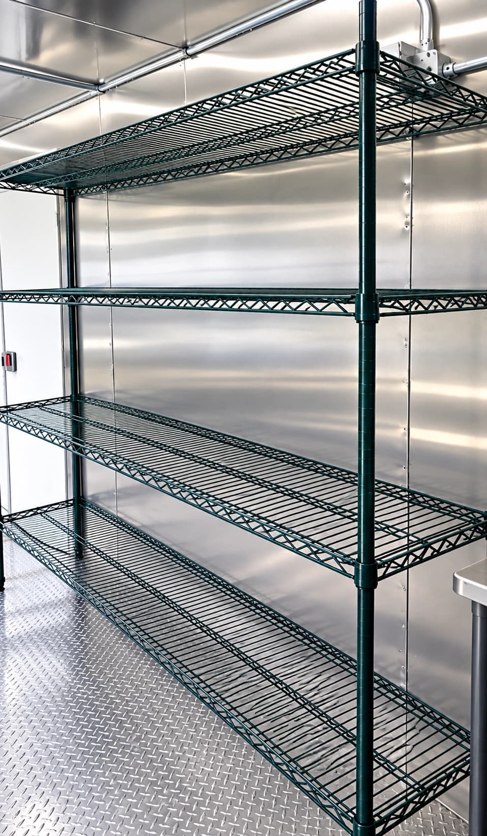 Freestanding wire shelving beside metal walls inside a dishwashing trailer