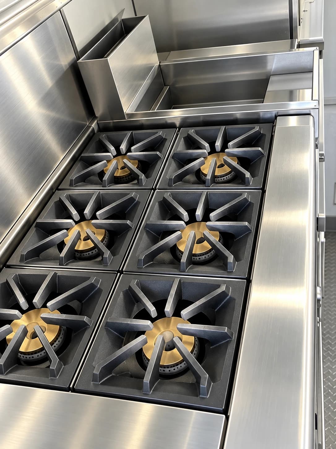 Six-burner commercial cooking range beneath a stainless-steel exhaust hood