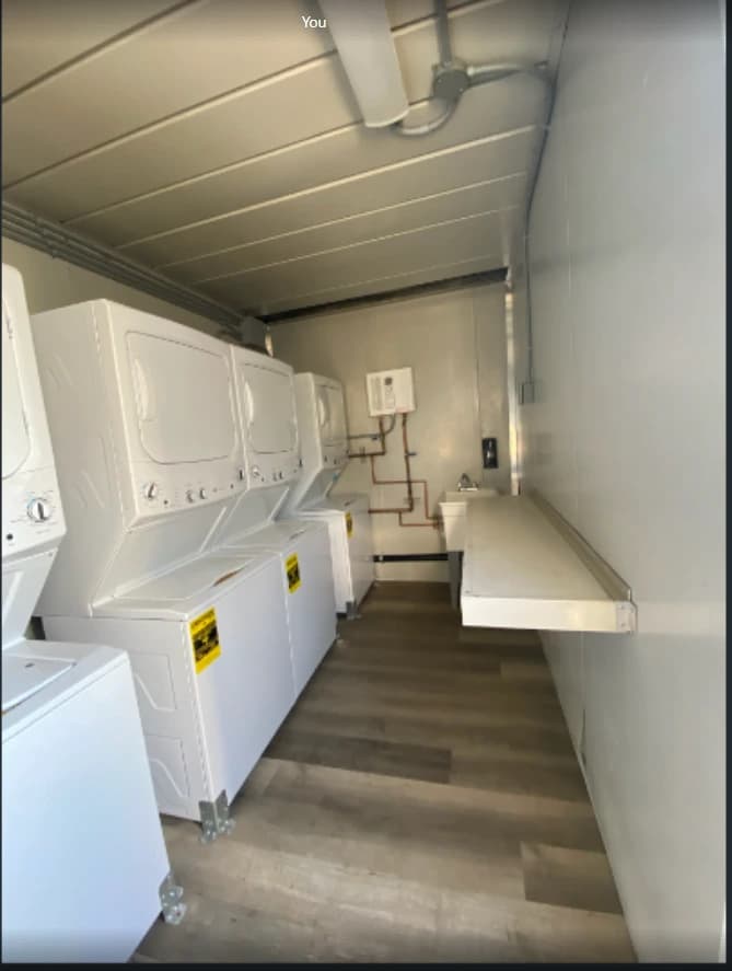 White laundry machines beside a narrow aisle and folding counter inside a container