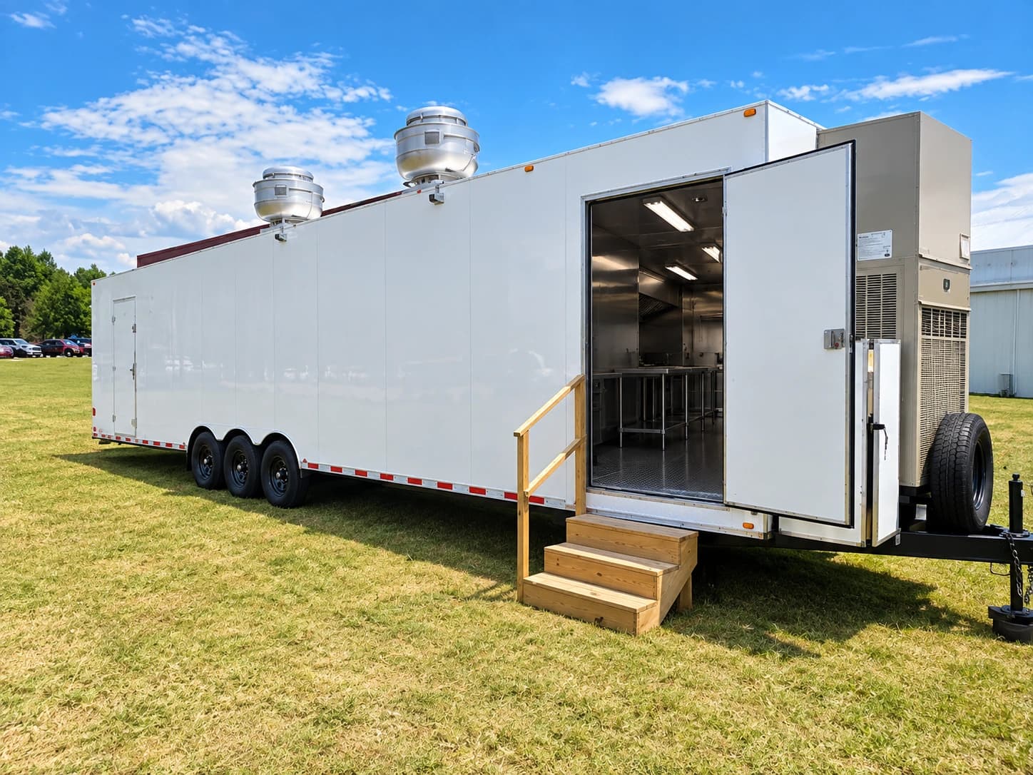 White kitchen trailer with rooftop exhaust fans, an open entrance and wooden entry steps