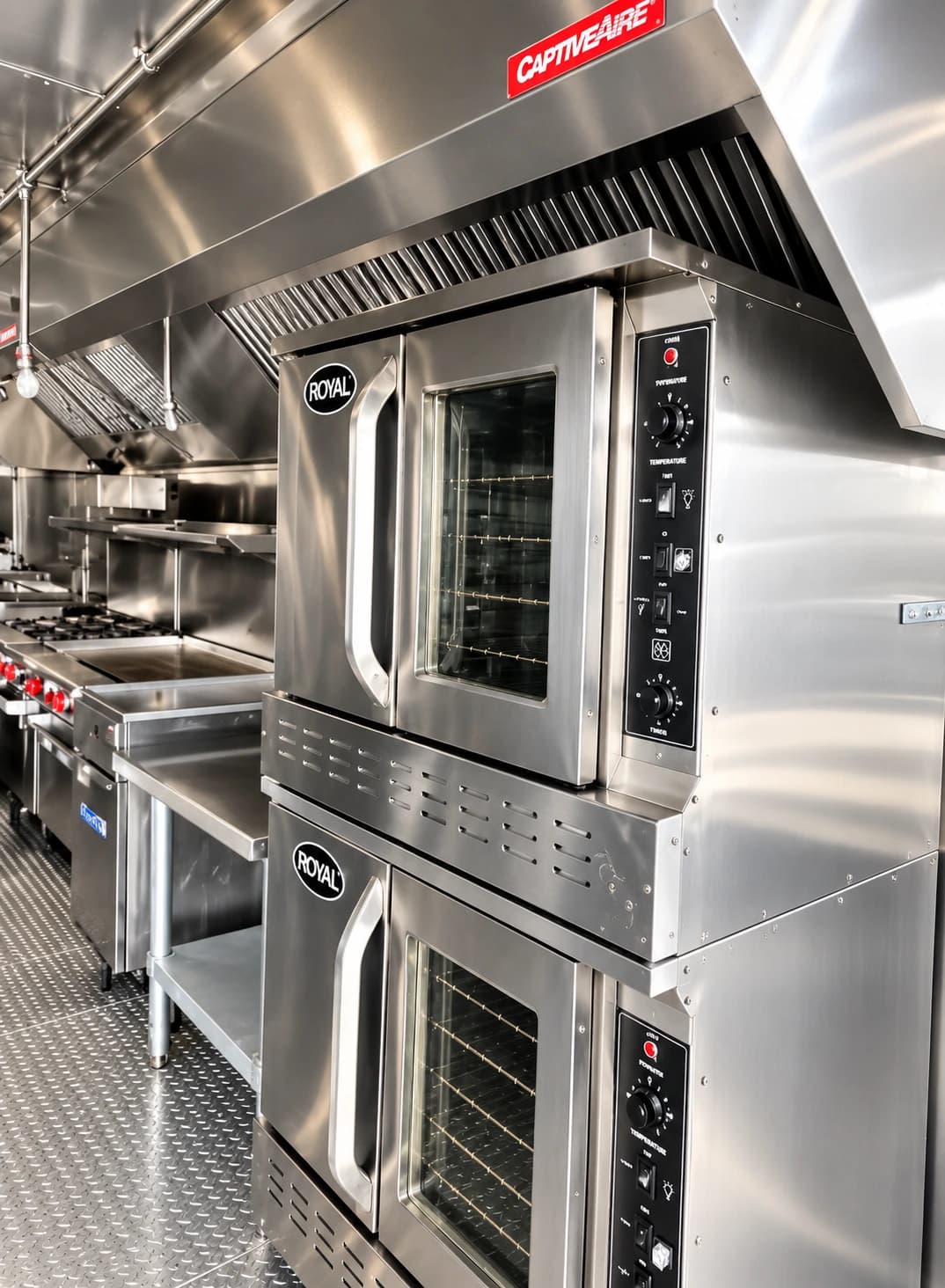 Stacked commercial ovens with glazed doors beneath a kitchen exhaust hood